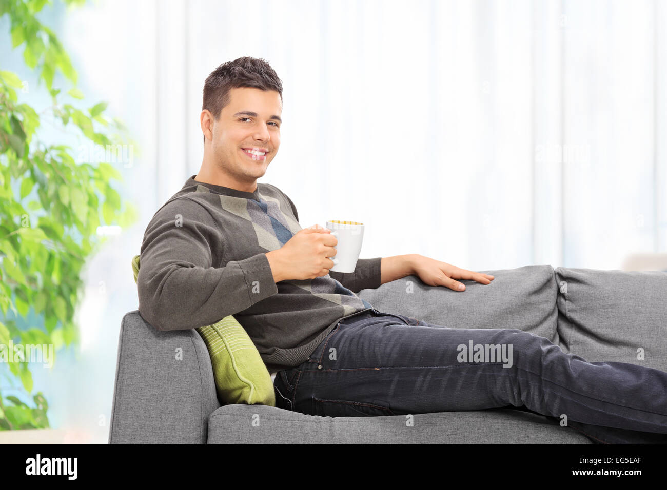 Young man drinking coffee seated on sofa at home Stock Photo