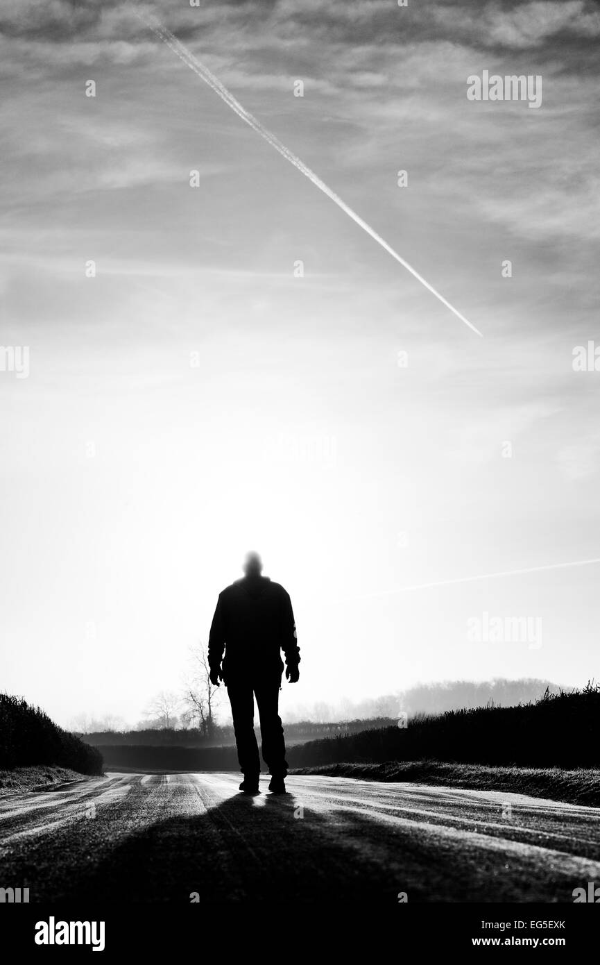 Man standing on a frost covered road in winter in front of the sun. Silhouette. UK Stock Photo