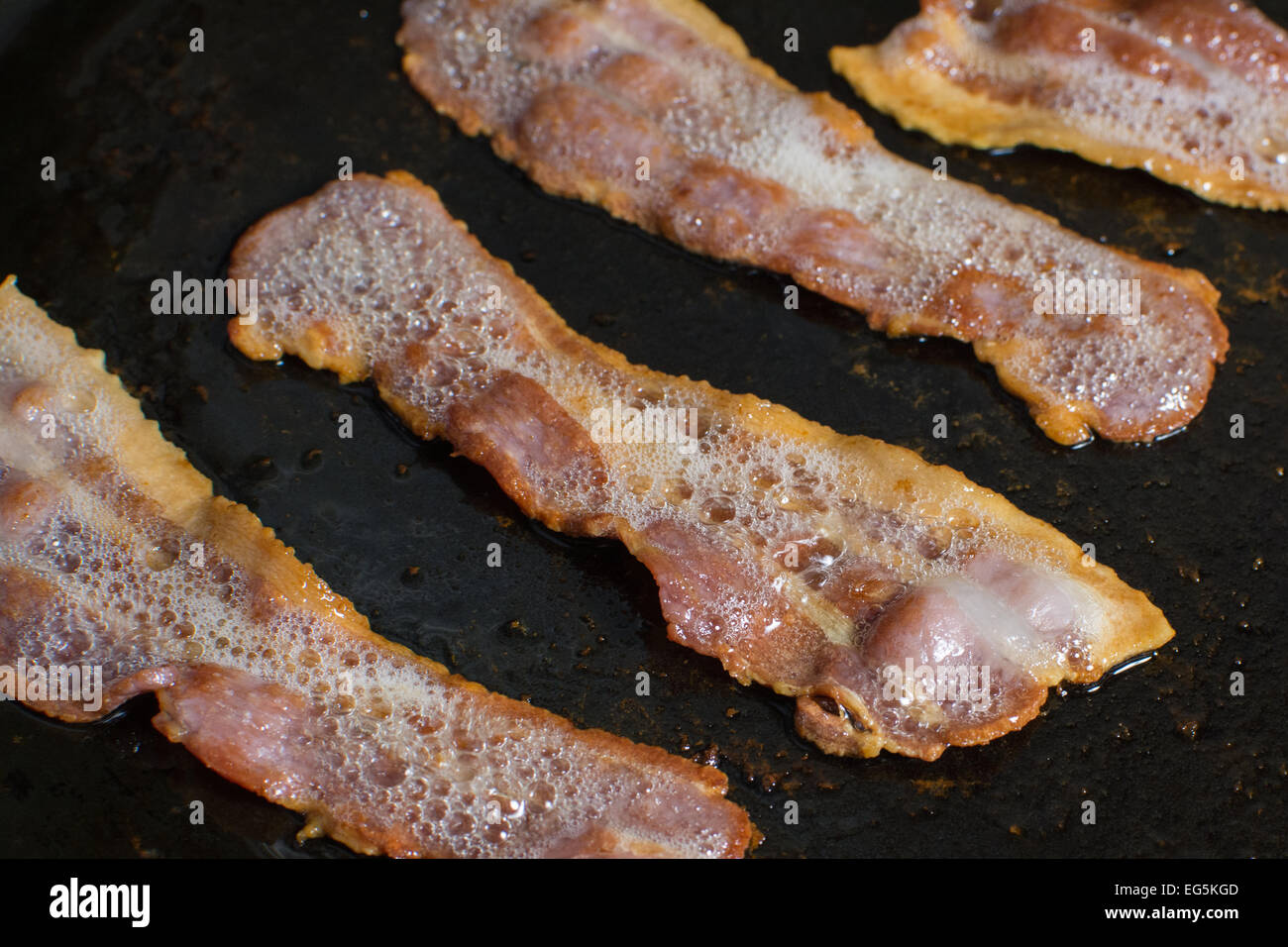 bacon frying and sizzling in a skillet Stock Photo