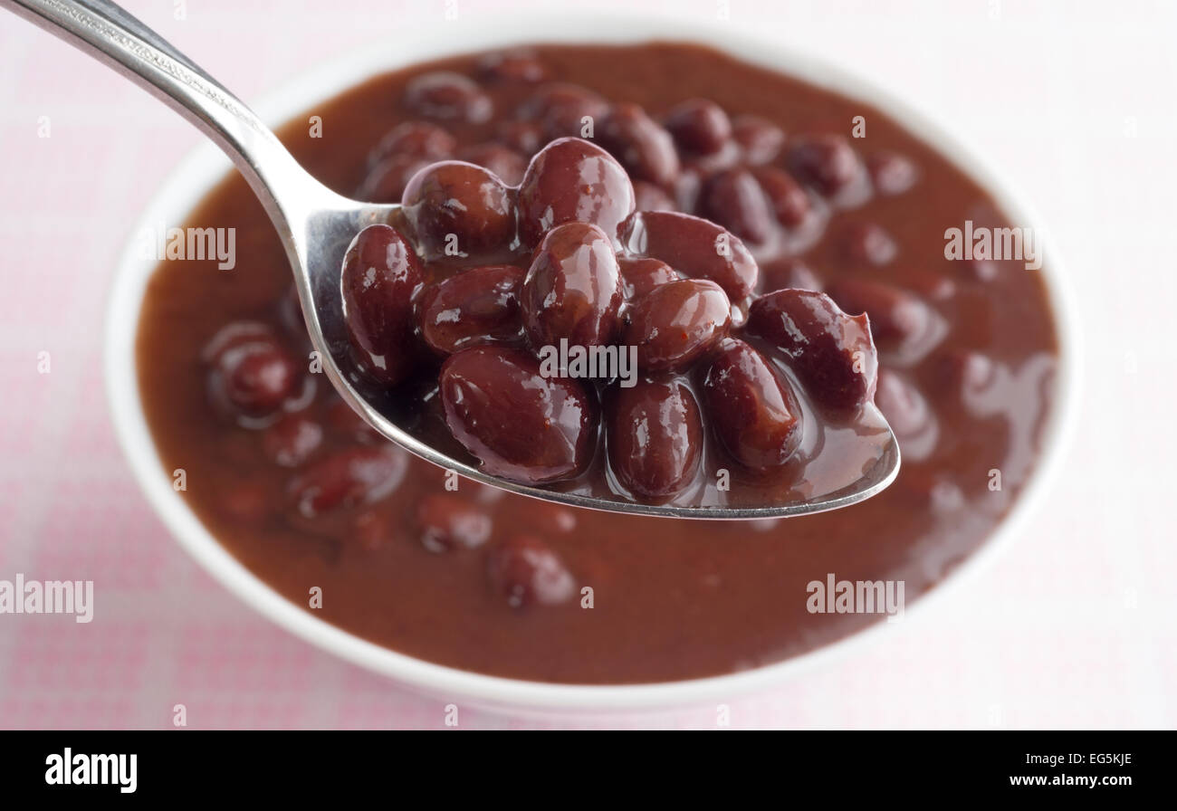 A spoon filled with black beans in a chili sauce with a bowl in the
