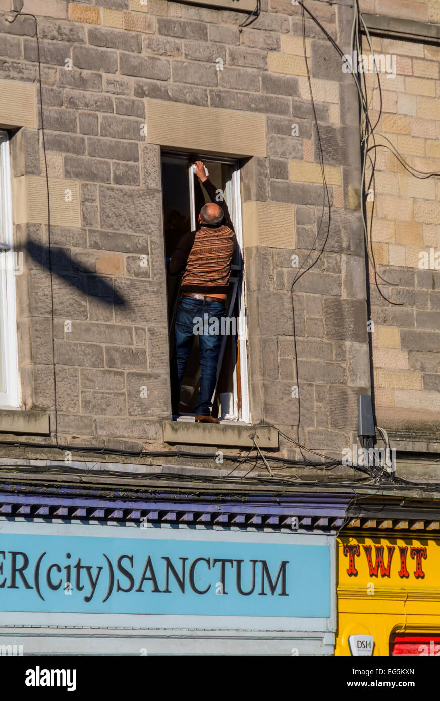 Cleaning windows without the use of a ladder - this man has ducked out to stand on a first floor window sill. Stock Photo
