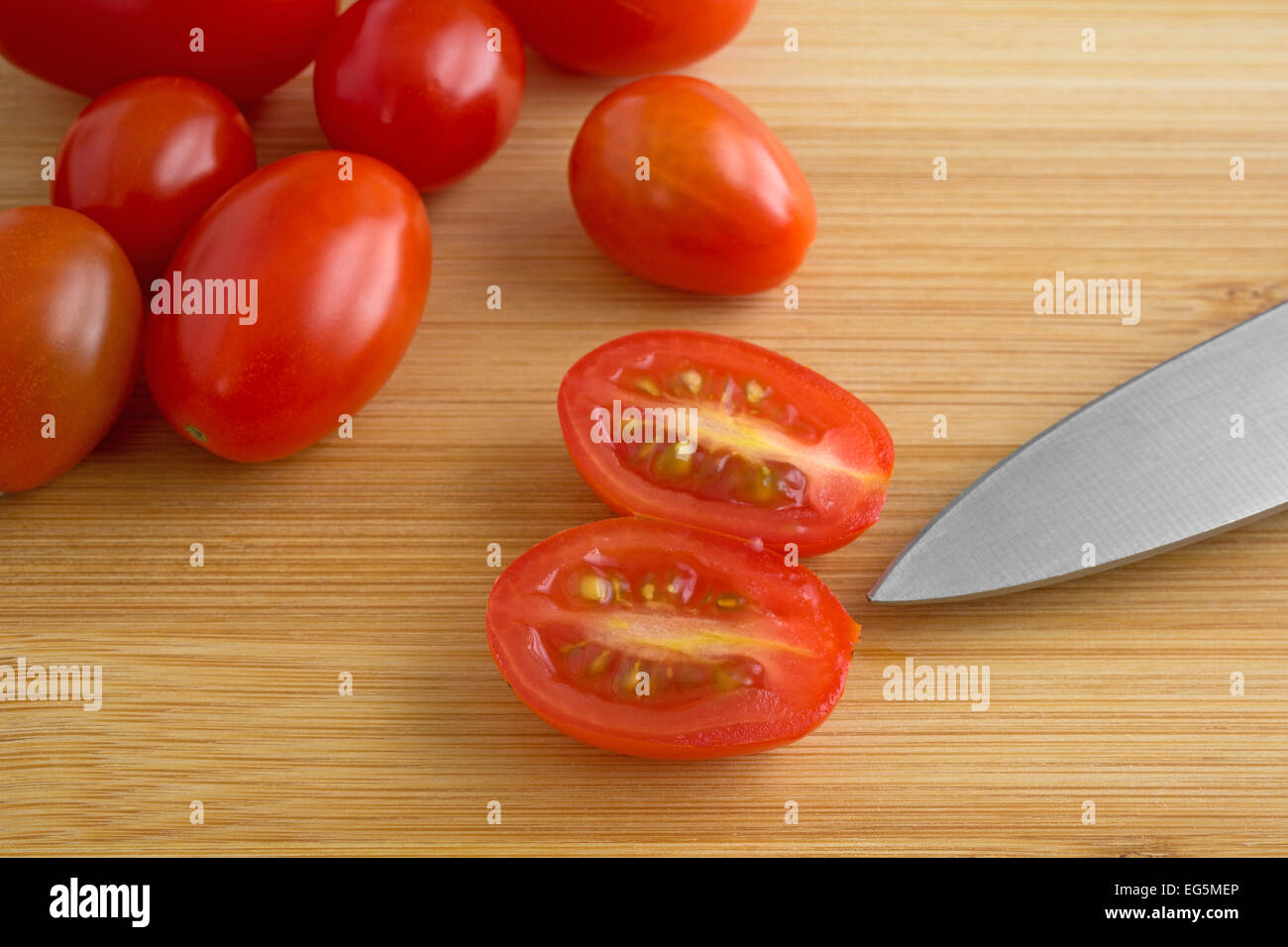 Several grape tomatoes on a wood cutting board with the end of a sharp ...