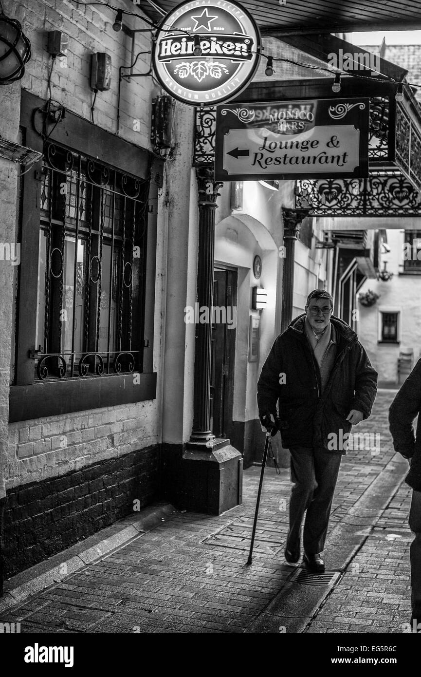 A man using a walking stick as he leaves Winecellar Entry Belfast.  The photograph is rendered as a monochrome Stock Photo