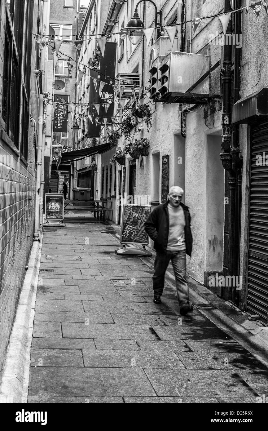 A man walking through Winecellar Entry Belfast.  The photograph is rendered as a monochrome. Stock Photo