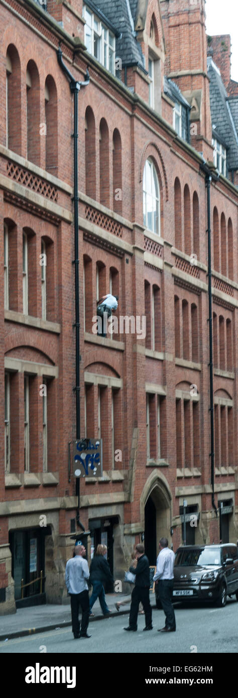 Window cleaner on very narrow ledge 3storeys up with no safety gear and man below oblivious to what is above him Stock Photo