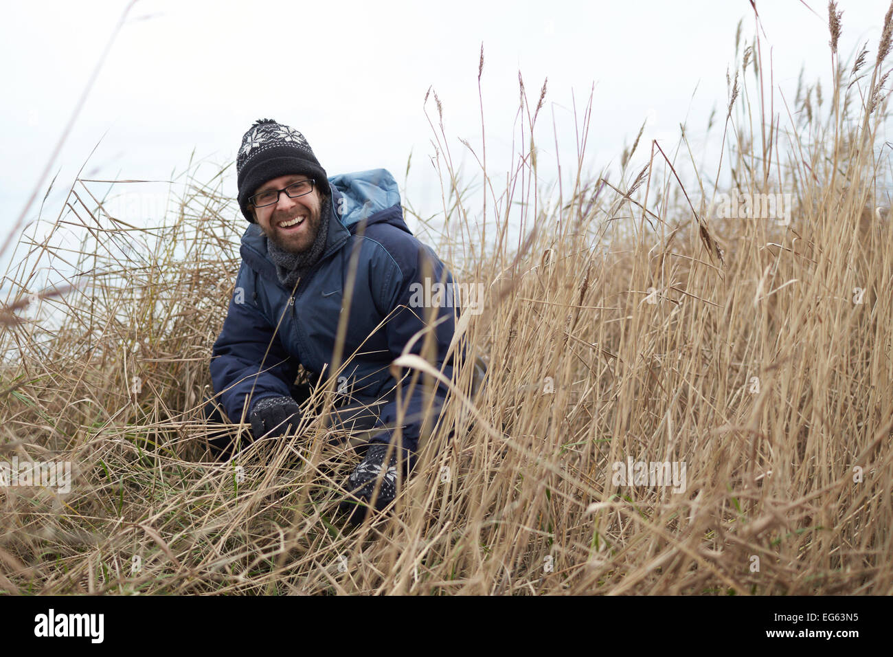 A portrait of a man laughing as he squats in long grasses Stock Photo