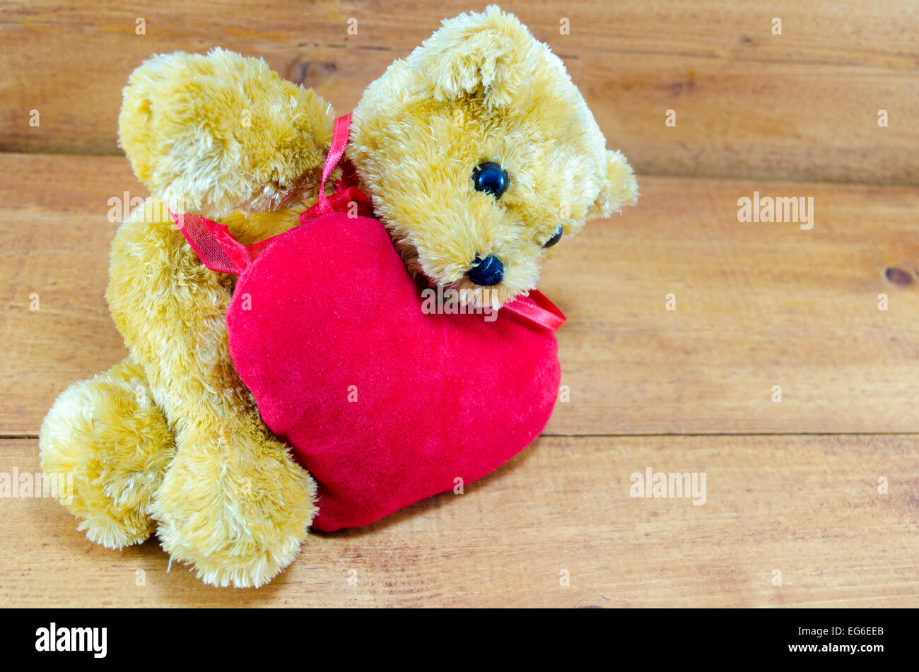 Big teddy bear lying on a red heart placed on a wooden table Stock Photo