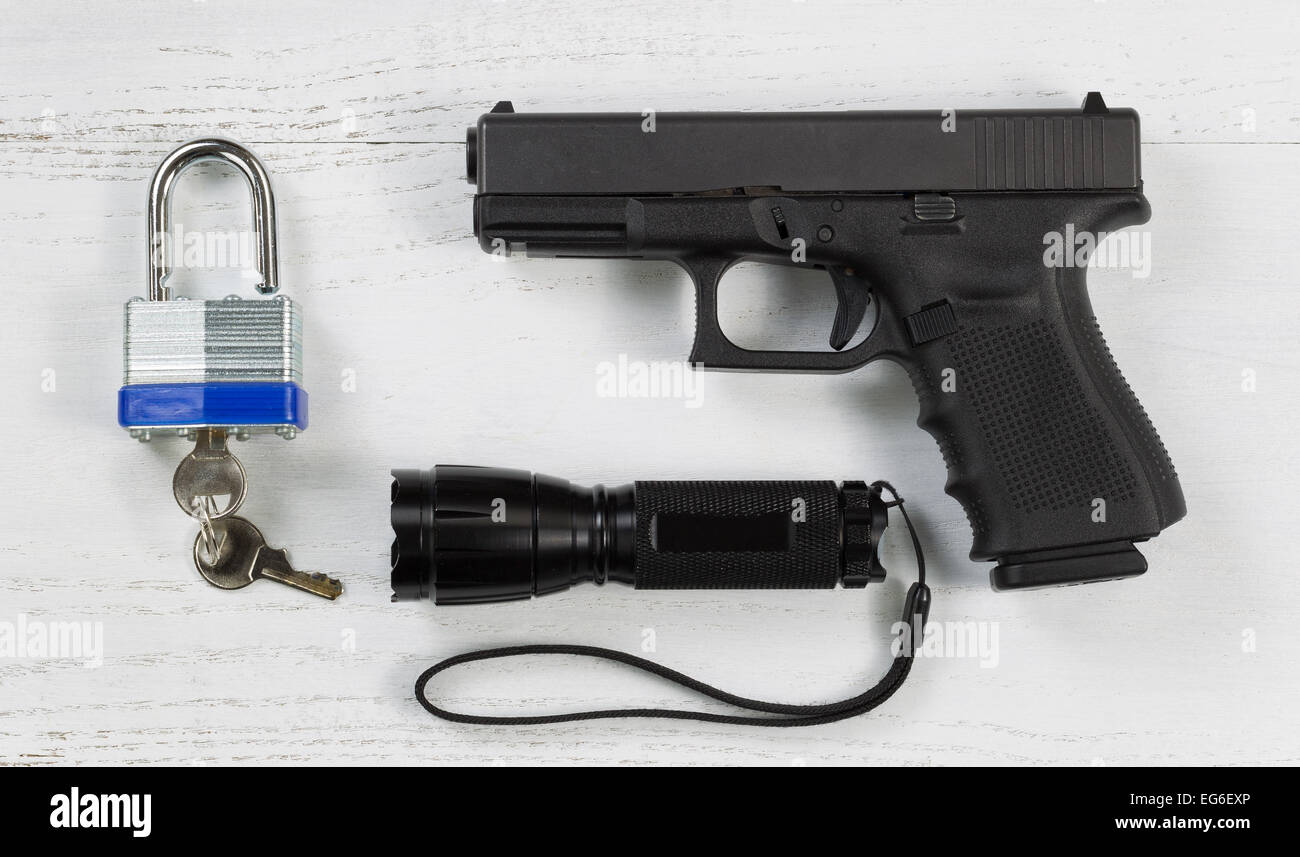 Overhead angled view of security items consisting of pistol, flashlight, and padlock with keys on white desktop. Stock Photo