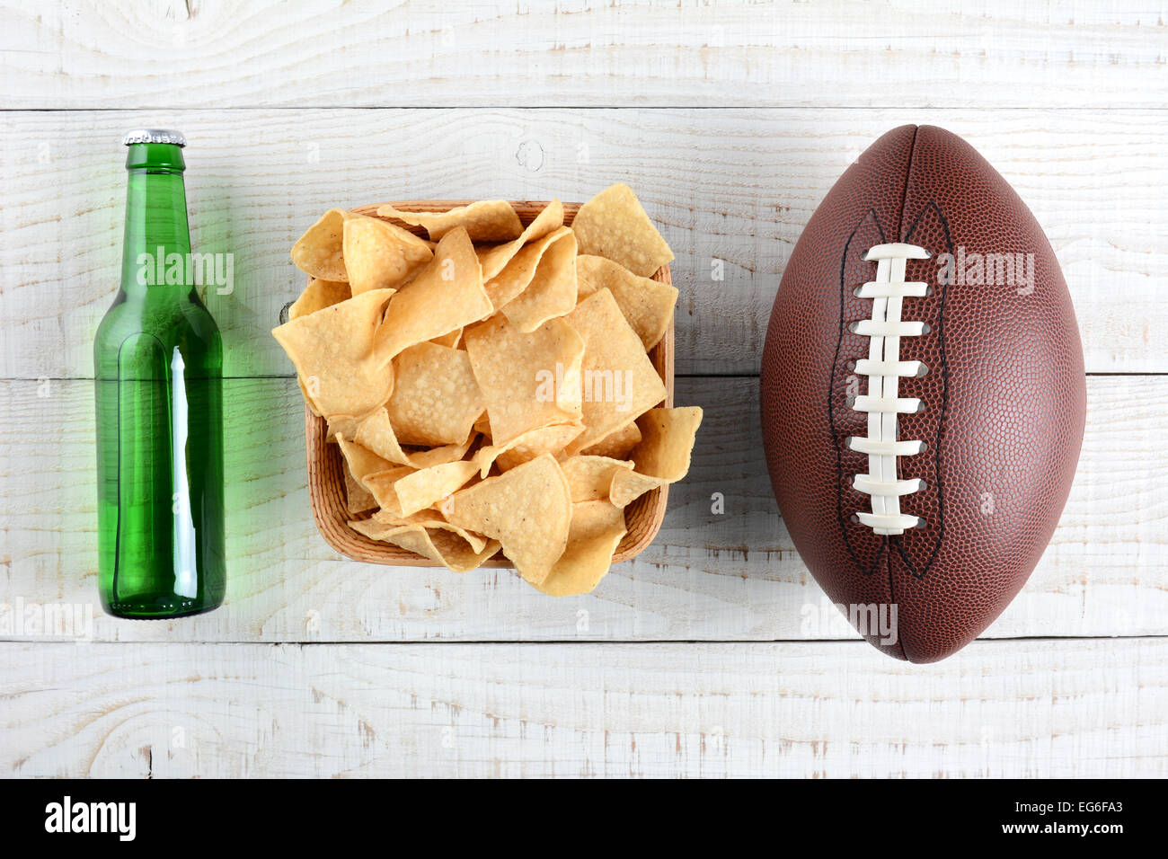 Beer bottle, bowl of chips and an American style football on a rustic whitewashed wood surface. Horizontal format. The bottle is Stock Photo