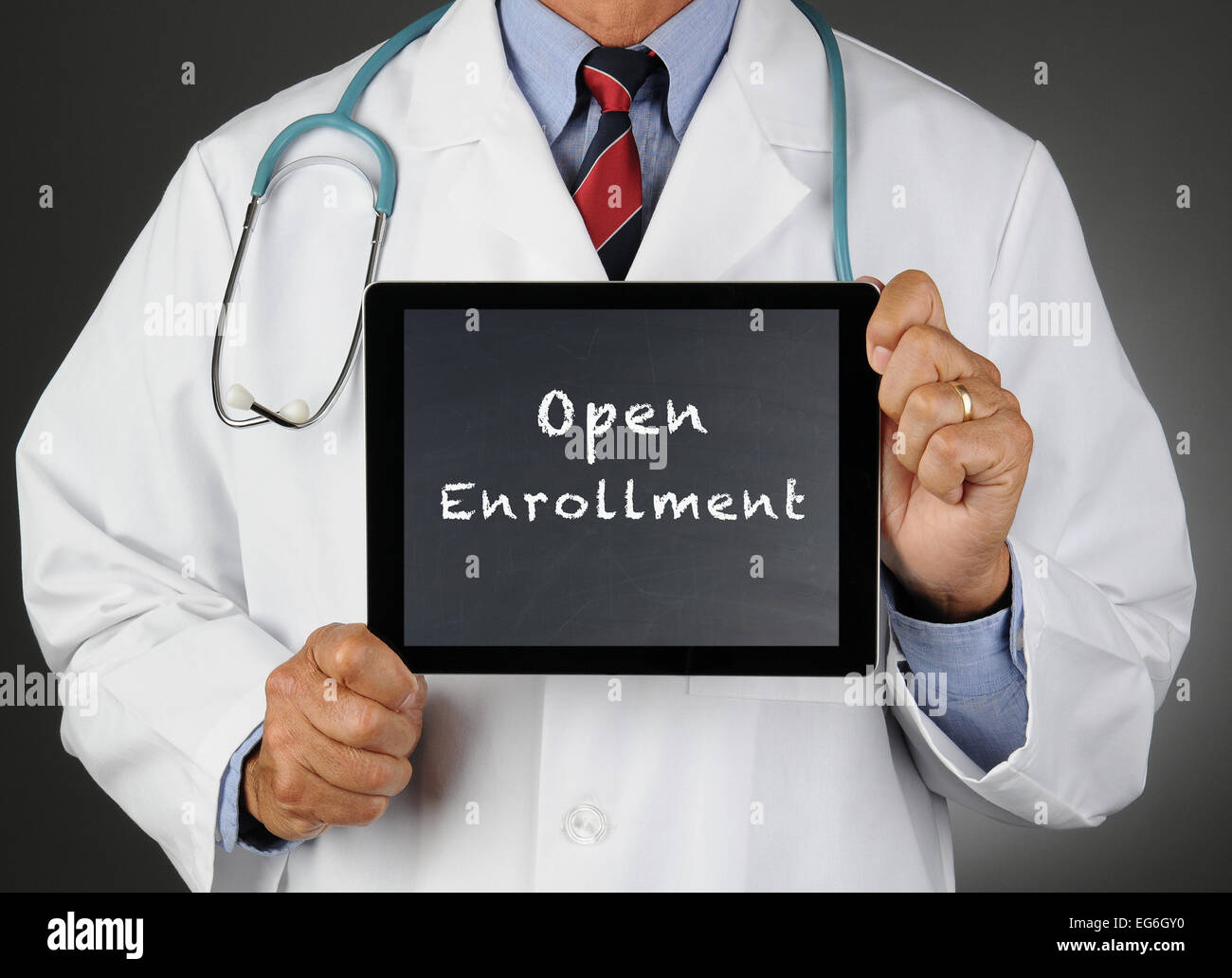 Closeup of a doctor holding a tablet computer with a chalkboard screen with the words Open Enrollment. Man is unrecognizable. Stock Photo