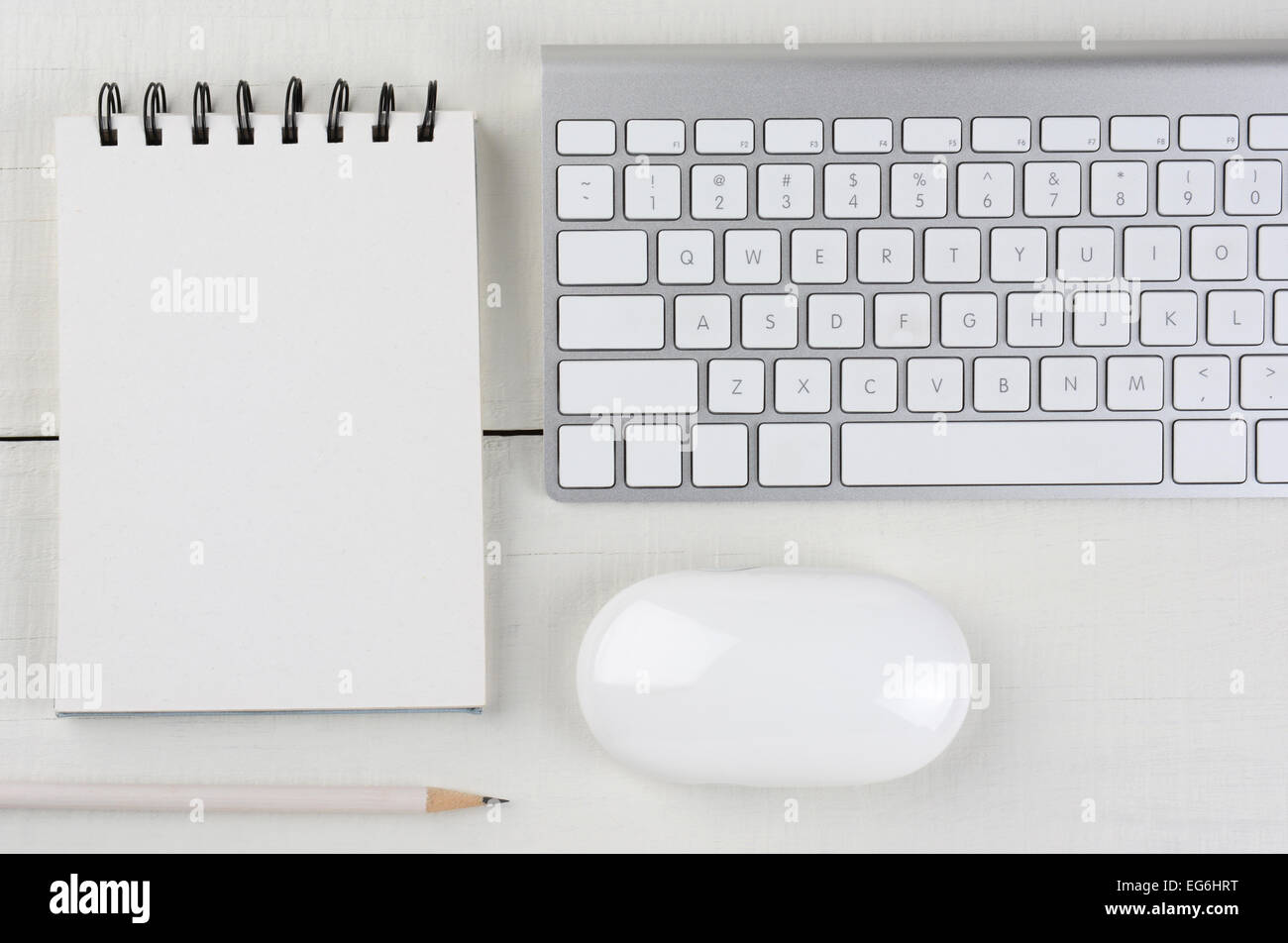 Horizontal image of a white wood home office desk with a computer keyboard, blank note pad, a white pencil, and mouse. Stock Photo