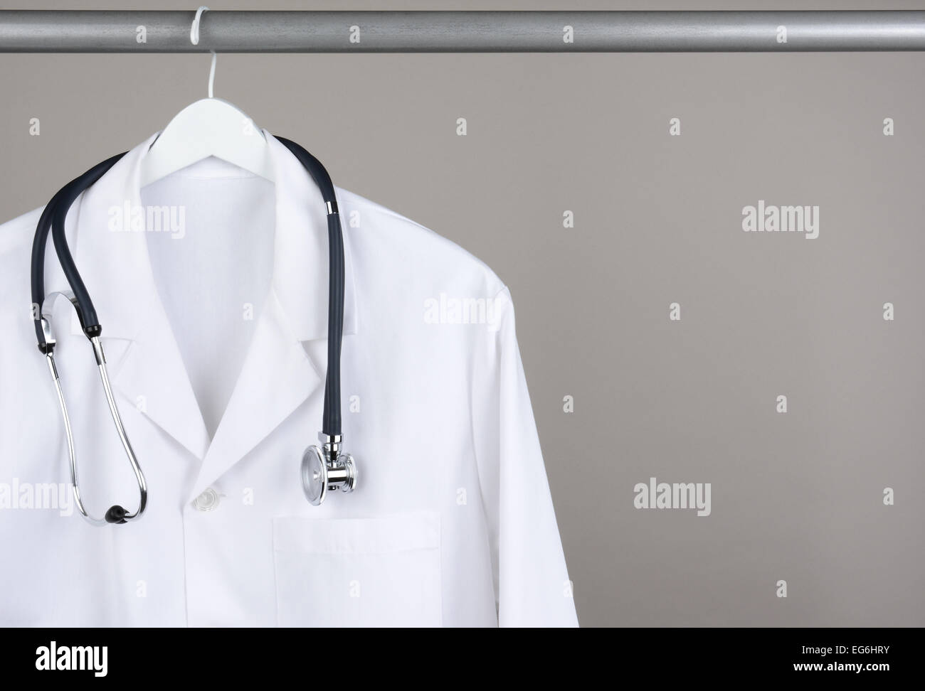 A doctor's lab coat and stethoscope on hanger against a gray background. Closeup on a white hanger with a gray background in hor Stock Photo