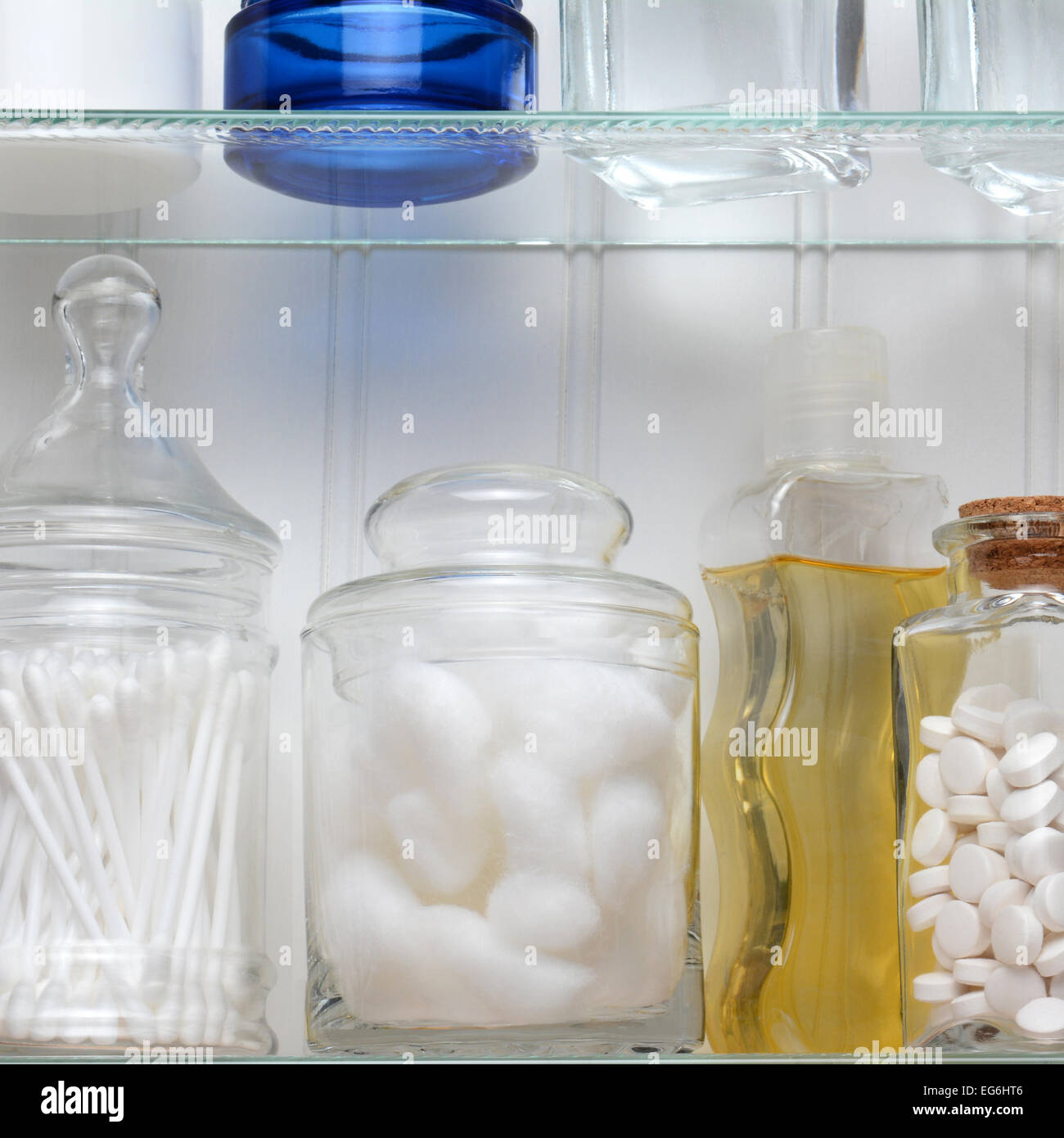 Closeup of two shelves of a medicine cabinet. A bottle of tablets, cotton balls and cotton swabs and assorted jars and bottles o Stock Photo