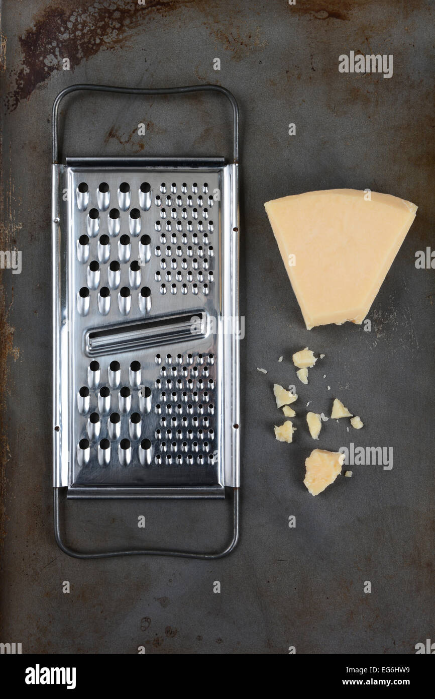 High angle shot of a broken wedge of Parmesan cheese and grater on used baking sheet. Vertical format. Stock Photo
