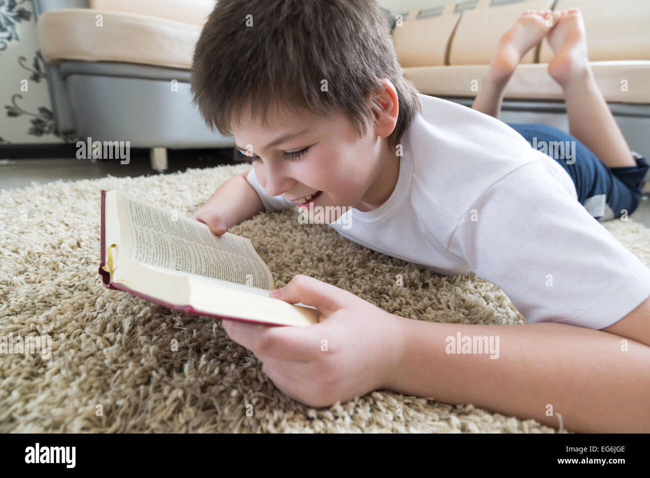 Boy reading a book while lying on  carpet in the room Stock Photo