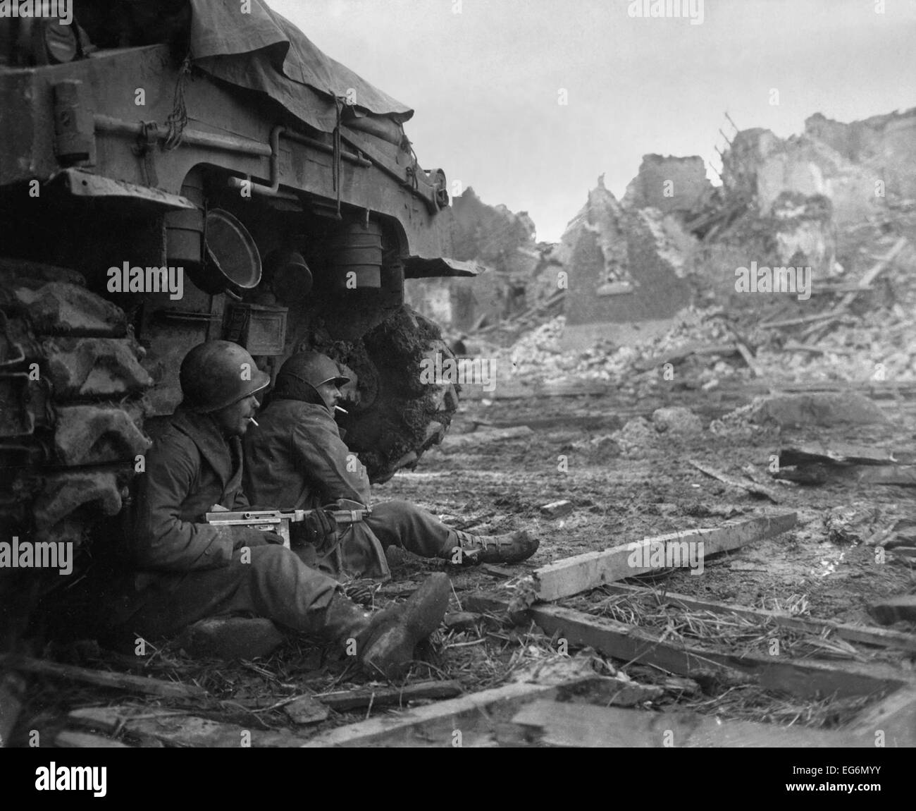 U.S. Infantrymen sheltering behind a M-4 Sherman tank during heavy German shelling. Dec. 11, 1944. Geich, Germany. World War 2. Stock Photo