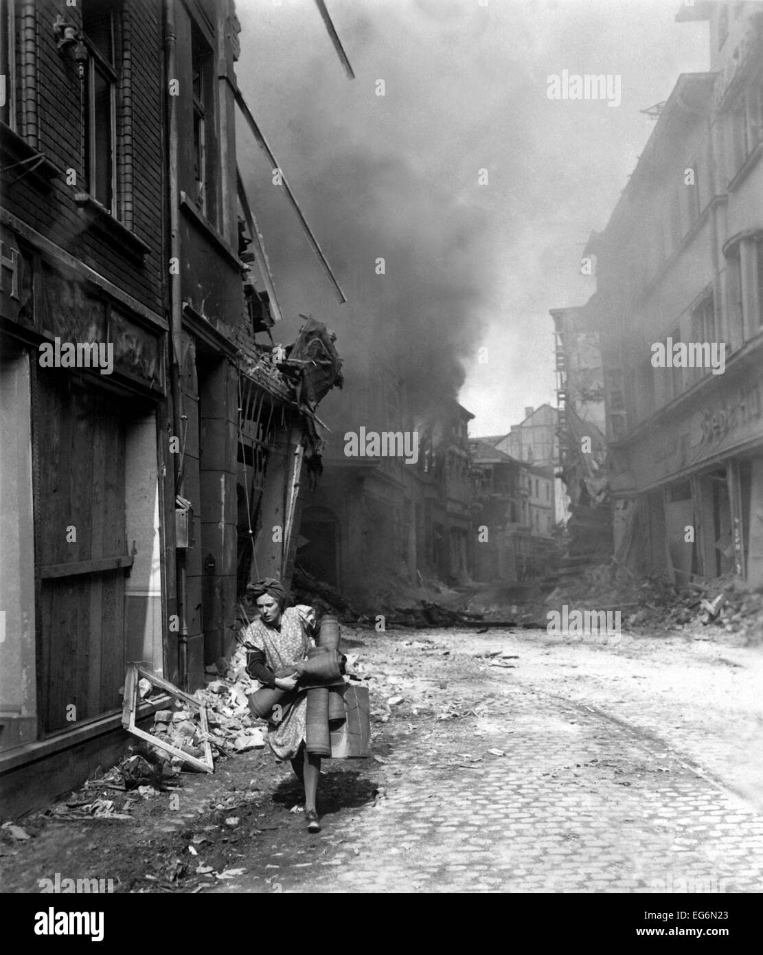 German woman runs from burning building carrying a suitcase and a few rugs. The fire was started in by Nazi saboteur in Stock Photo