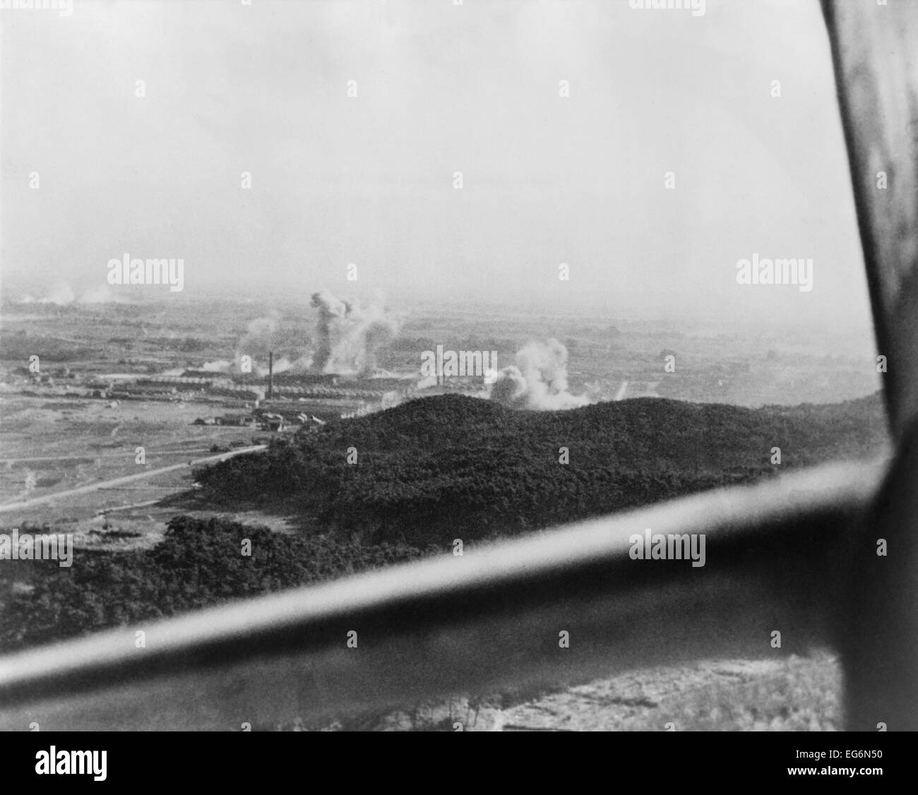 U.S. carrier-based planes bomb a factory plant near Tokyo in 1945. Framing the scene is the window of an American airplane. Stock Photo