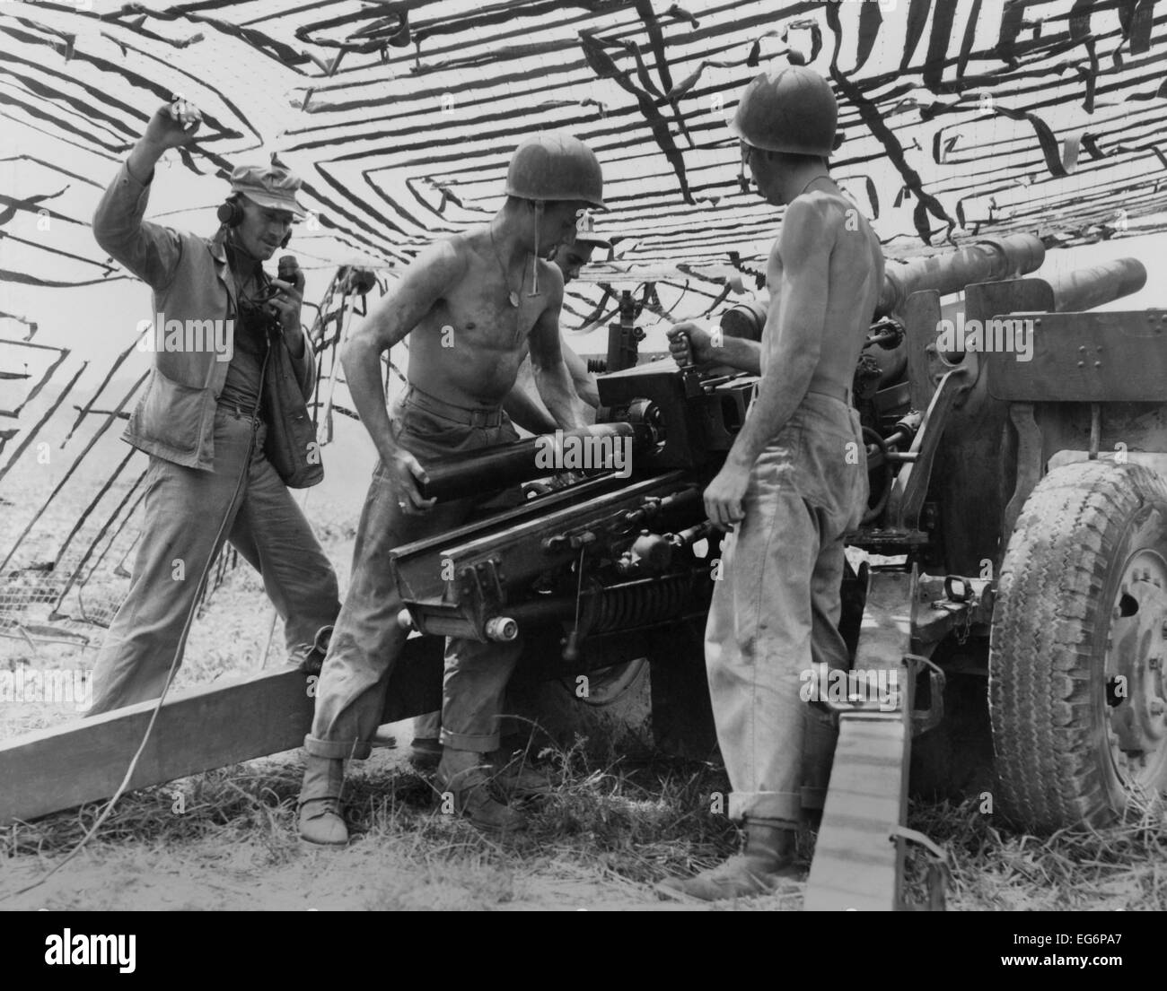 Four soldiers man U.S. Army 105 mm. artillery under a camouflage net in ...
