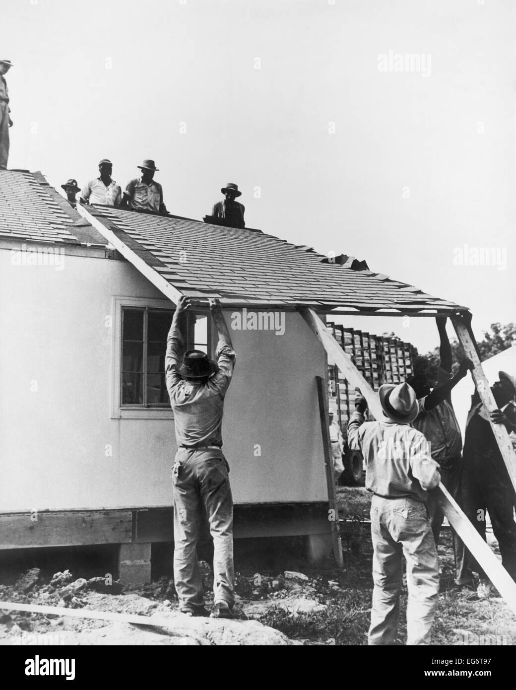 Men lifting a section of roof onto a prefabricated house, April 13 ...