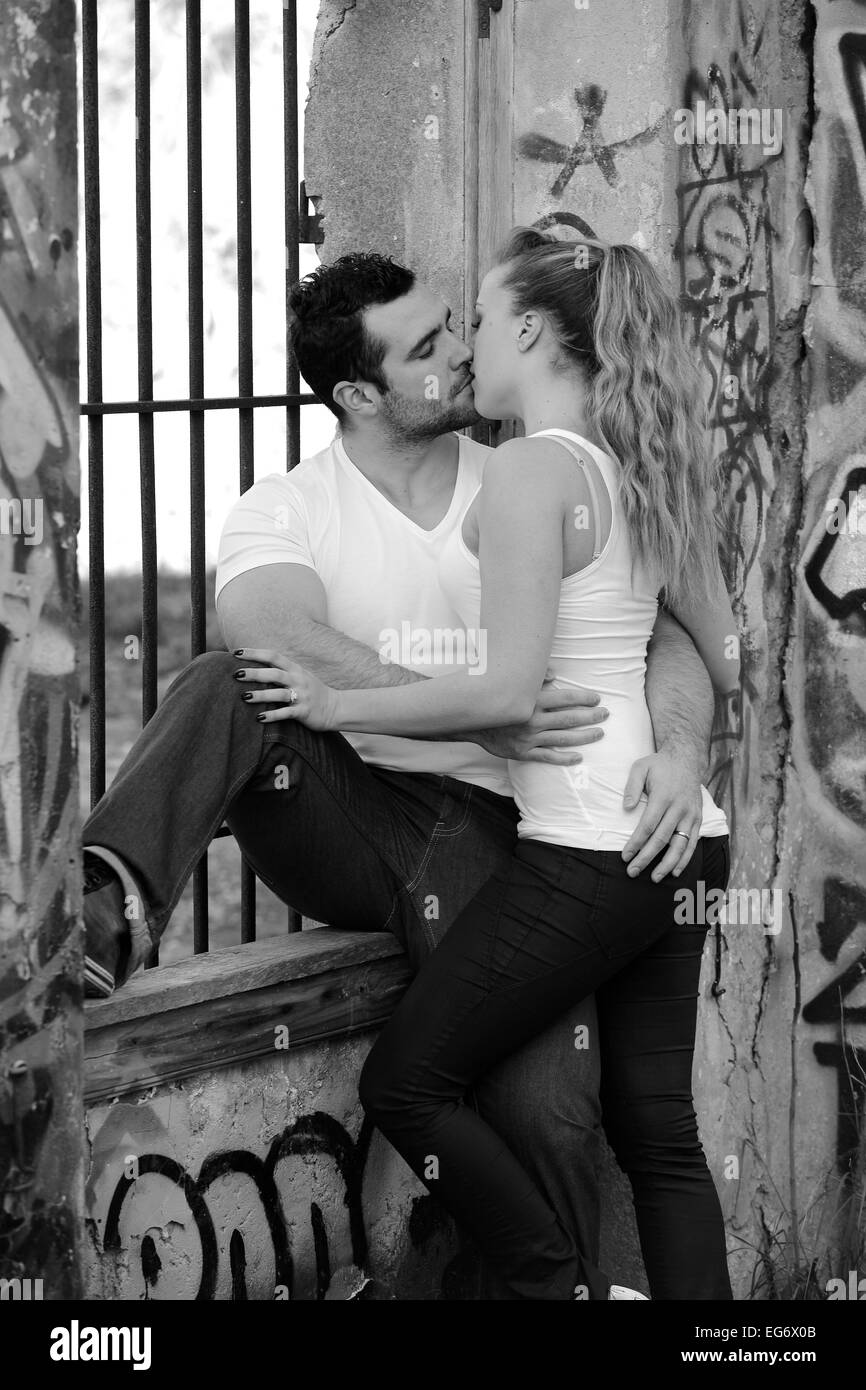 Young couple kissing at a barred window in a ruined building covered in graffiti Stock Photo