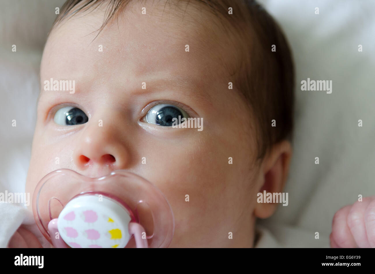 A newborn baby with a dummy lying down on white sheets Stock Photo