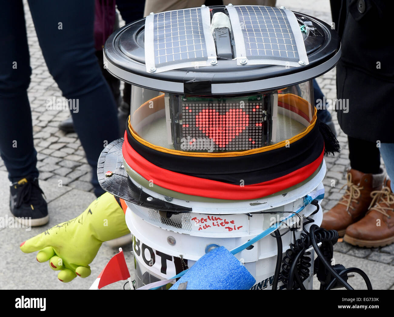 Berlin, Germany. 18th Feb, 2015. Robot 'hitchBOT' stands in front of the Brandenburg Gate with the writing 'Berlin I love you' on it, surrounded by tourists in Berlin, Germany, 18 February 2015. The robot is supposed to find out if a robot can rely on the cooperation of people. It can have conversations independently but is incapable of moving and is dependent of people taking it by car. Photo: JENS KALAENE/dpa/Alamy Live News Stock Photo