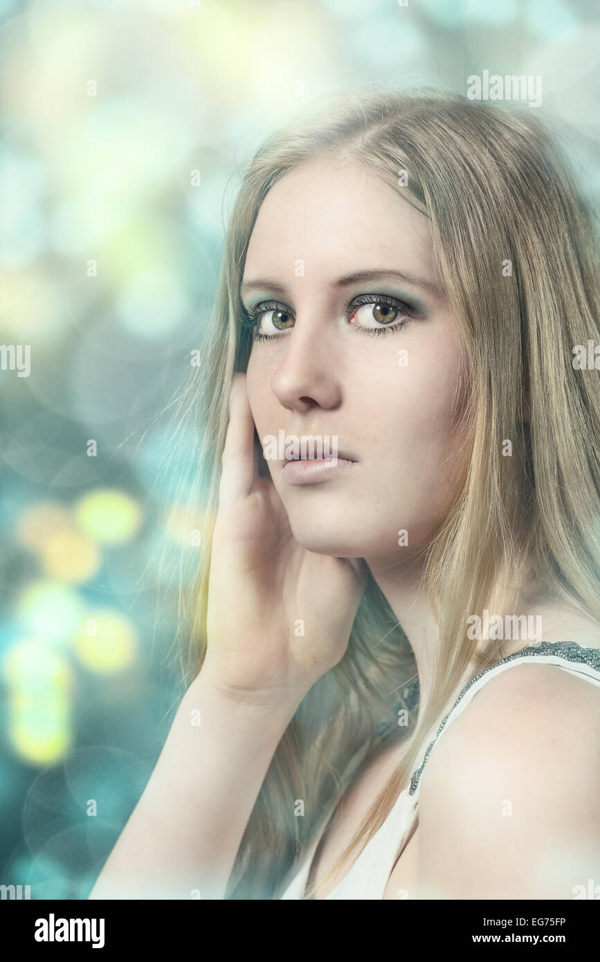 Close up Portrait of Pretty Young Blond Woman with her hand to her face While Looking at the Camera on Abstract Background Stock Photo