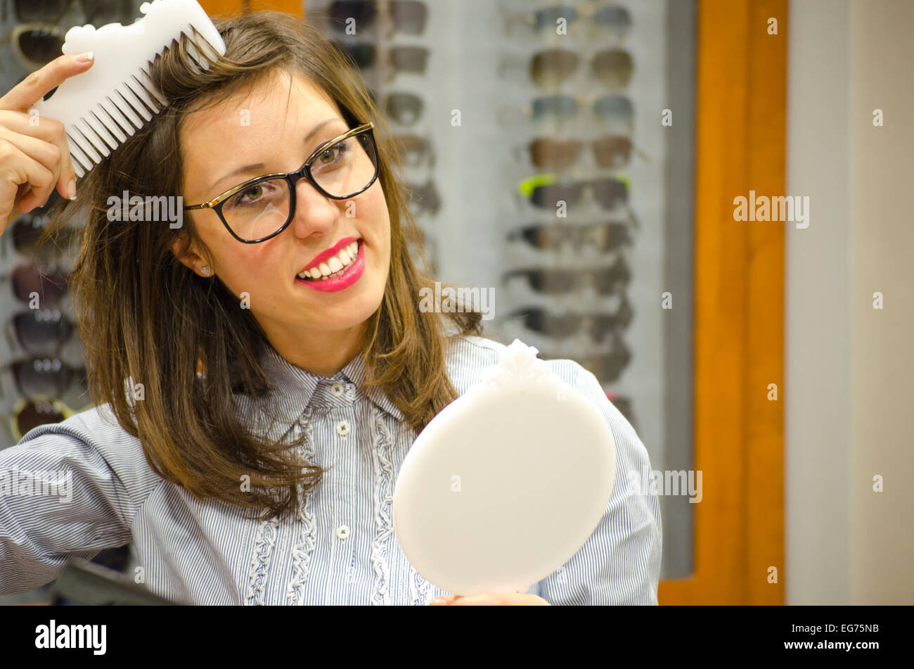 Young brunette trying red glasses at the optics store with different frames in the background Stock Photo