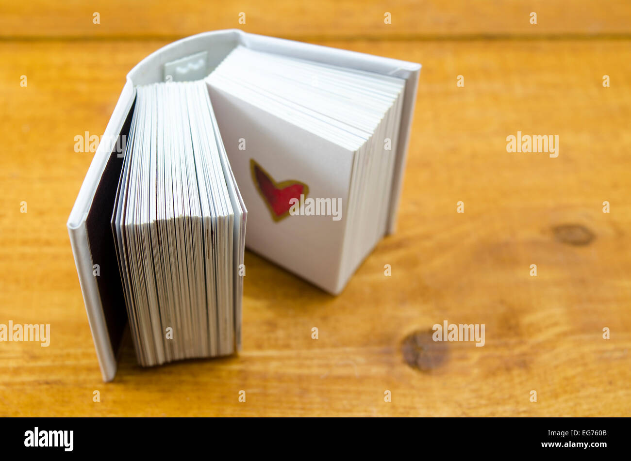 Small open book with a heart shape on a page, shot against a wooden surface Stock Photo