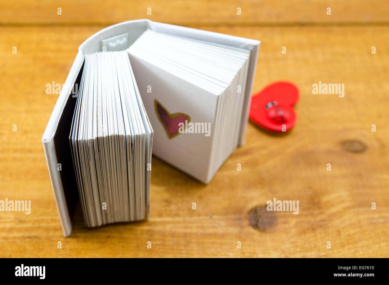 Small open book with a heart shape on a page, shot against a wooden surface Stock Photo
