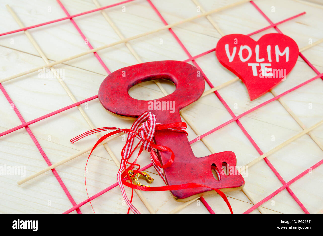 Red symbolic vintage key on wooden surface with a wooden heart saying I love you in Serbo-Croatian Stock Photo