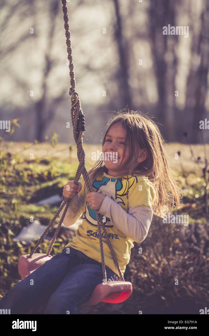 Smiling little girl sitting on a swing Stock Photo - Alamy