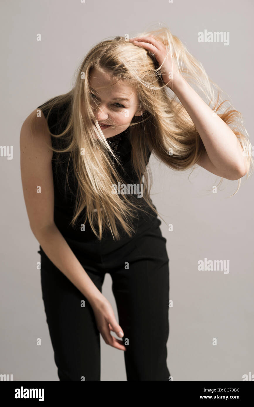 Smiling blond woman with hand in her hair in front of grey background Stock Photo