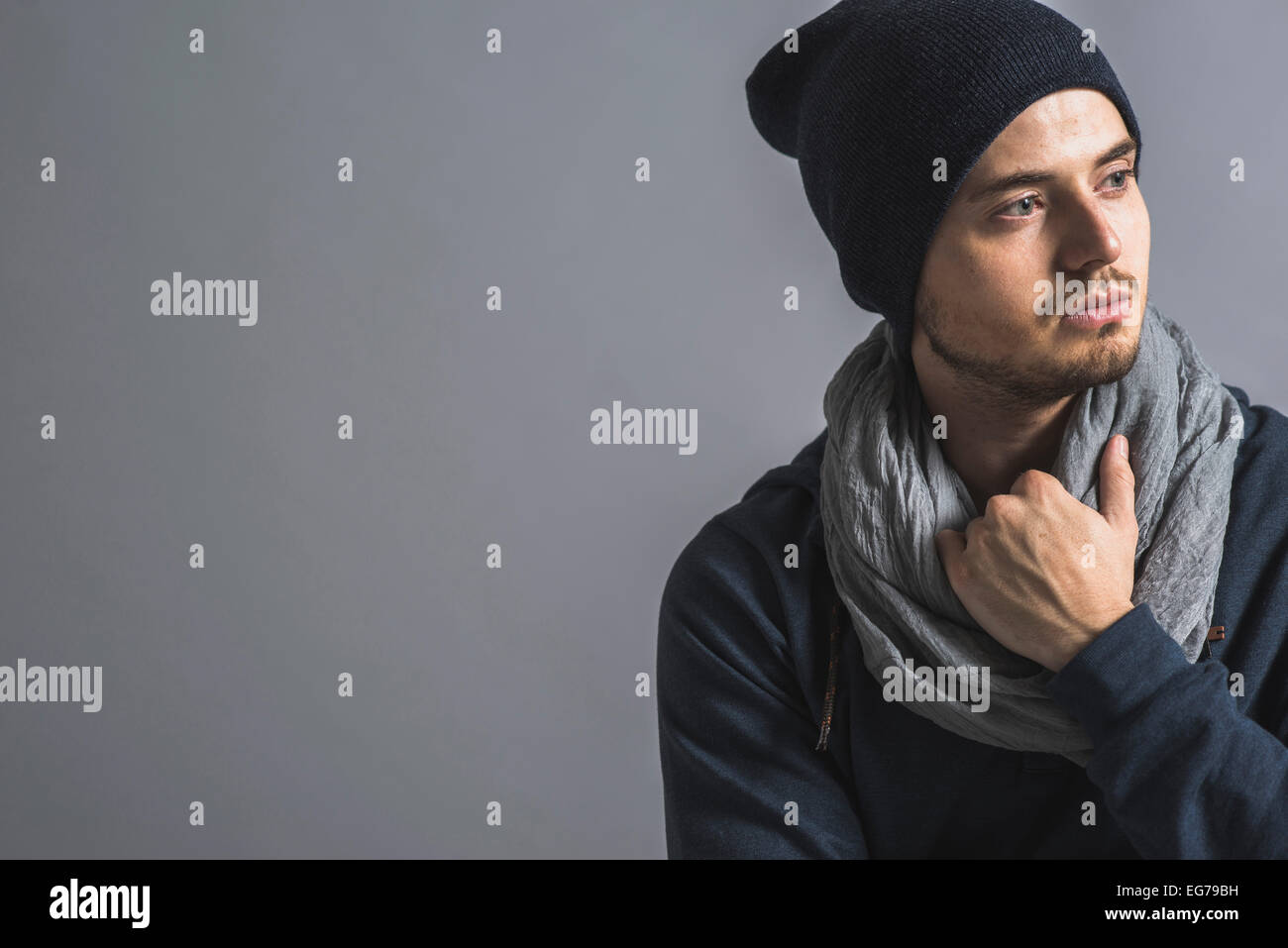 Portrait of pensive young man wearing wool cap and scarf in front of grey background Stock Photo