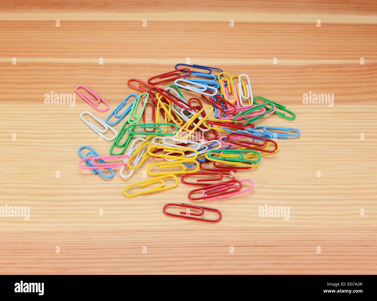 Pile of small coloured paper clips on a wooden background Stock Photo