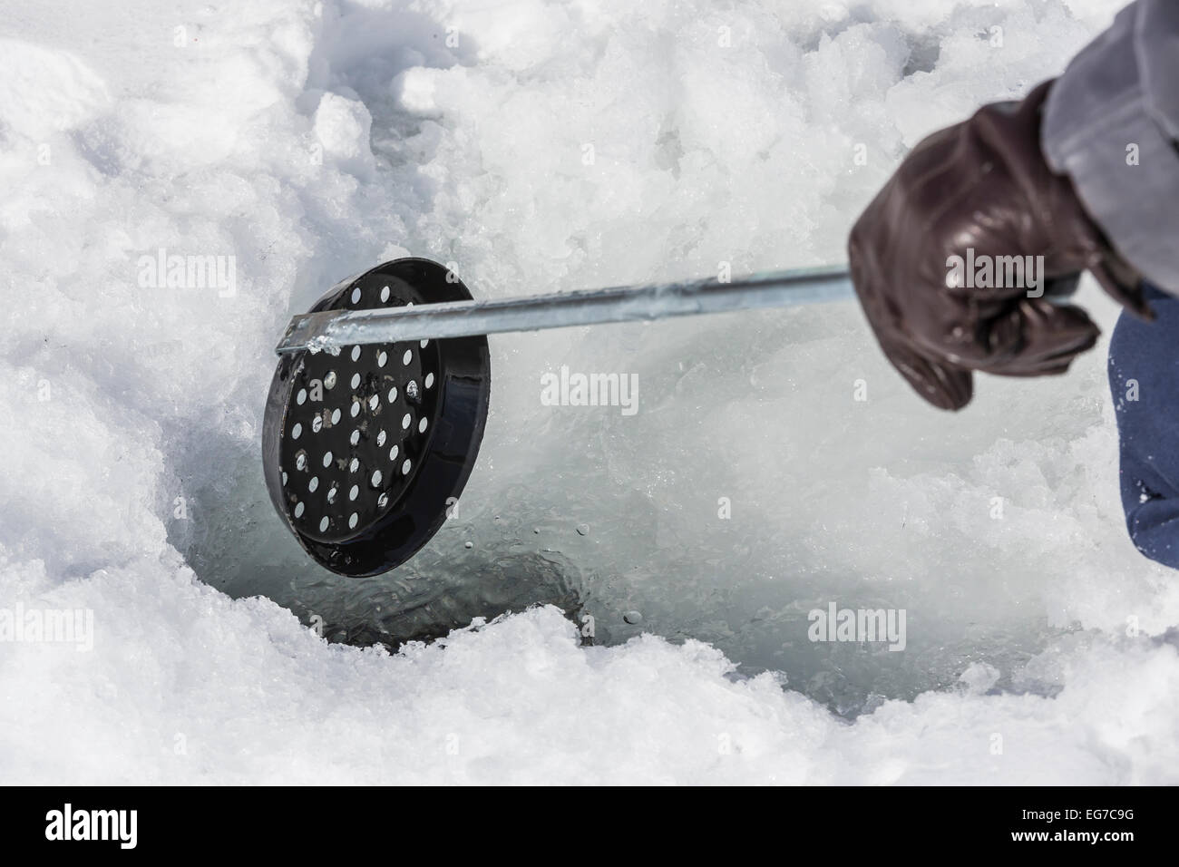 Using a skimmer to remove ice from an ice fishing hole drilled by an ice  auger on a lake in central Michigan, USA Stock Photo - Alamy