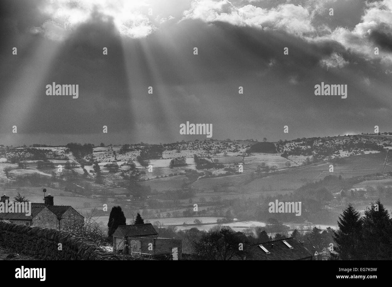 Black and white view of sun rays bursting through the clouds over snowy fields near Darley Dale in the Peak District Stock Photo