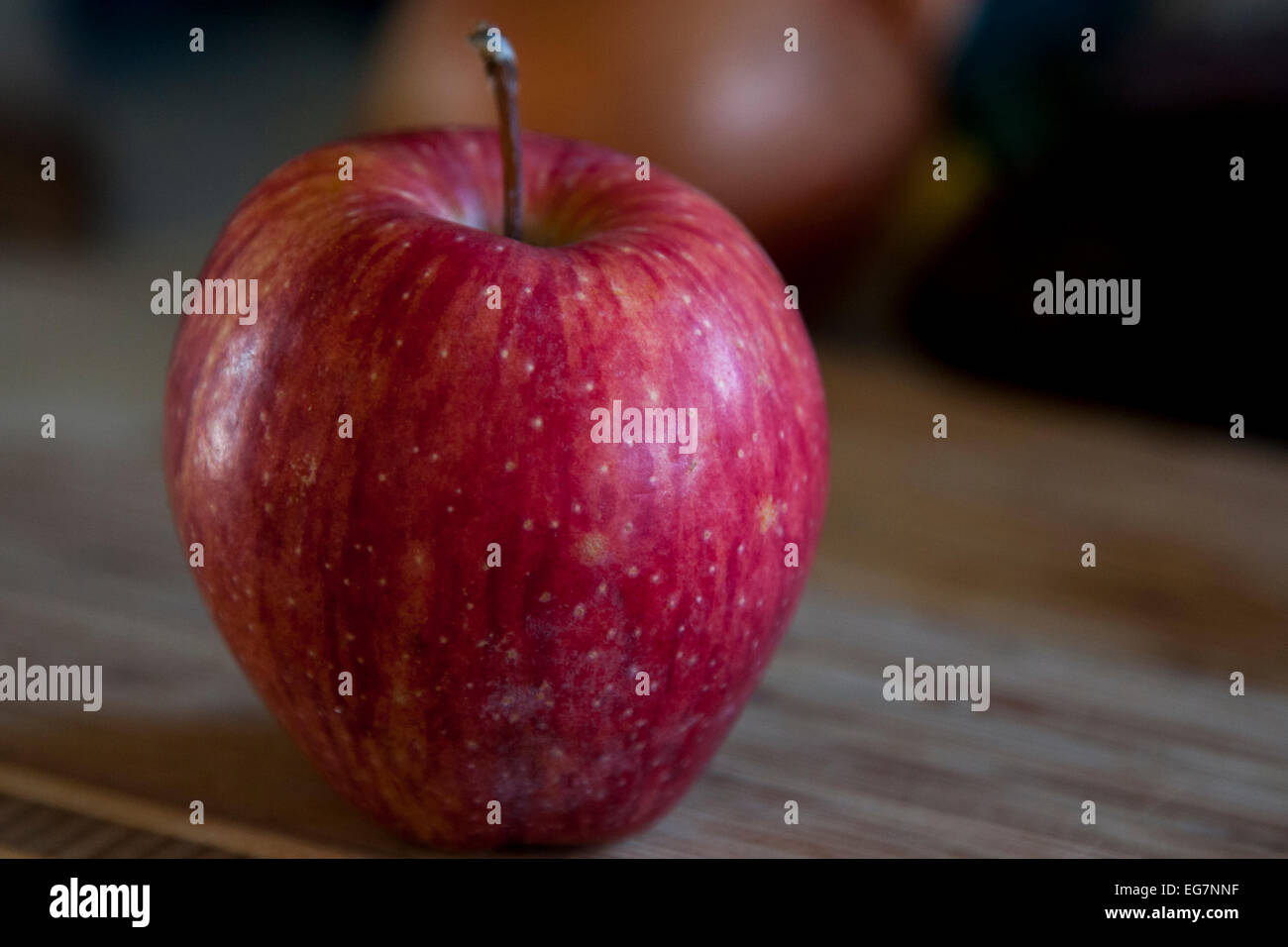 Organic red apple sitting on a bamboo cutting board. Stock Photo