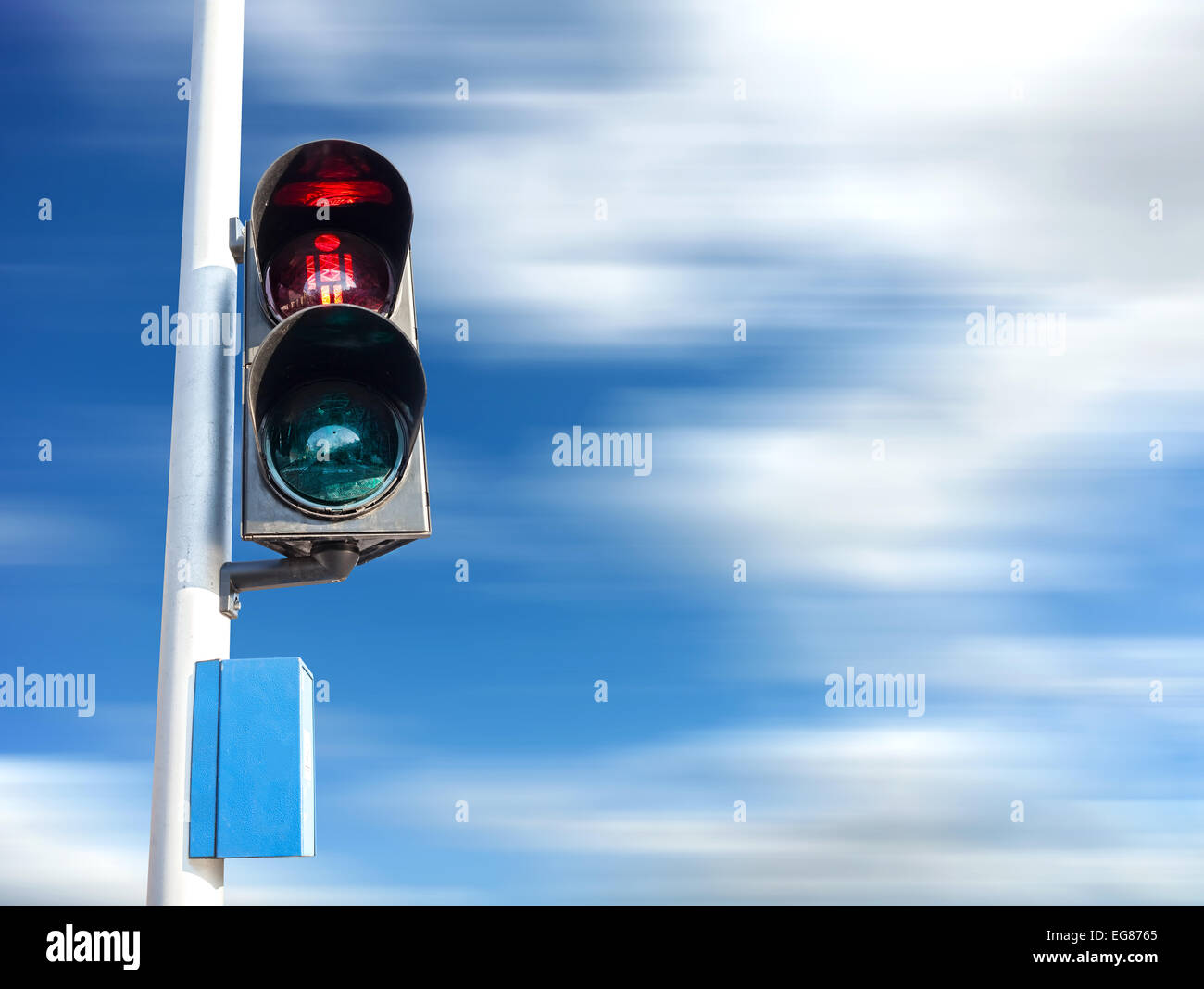 Red color on the traffic light for pedestrian, motion blurred sky. Stock Photo