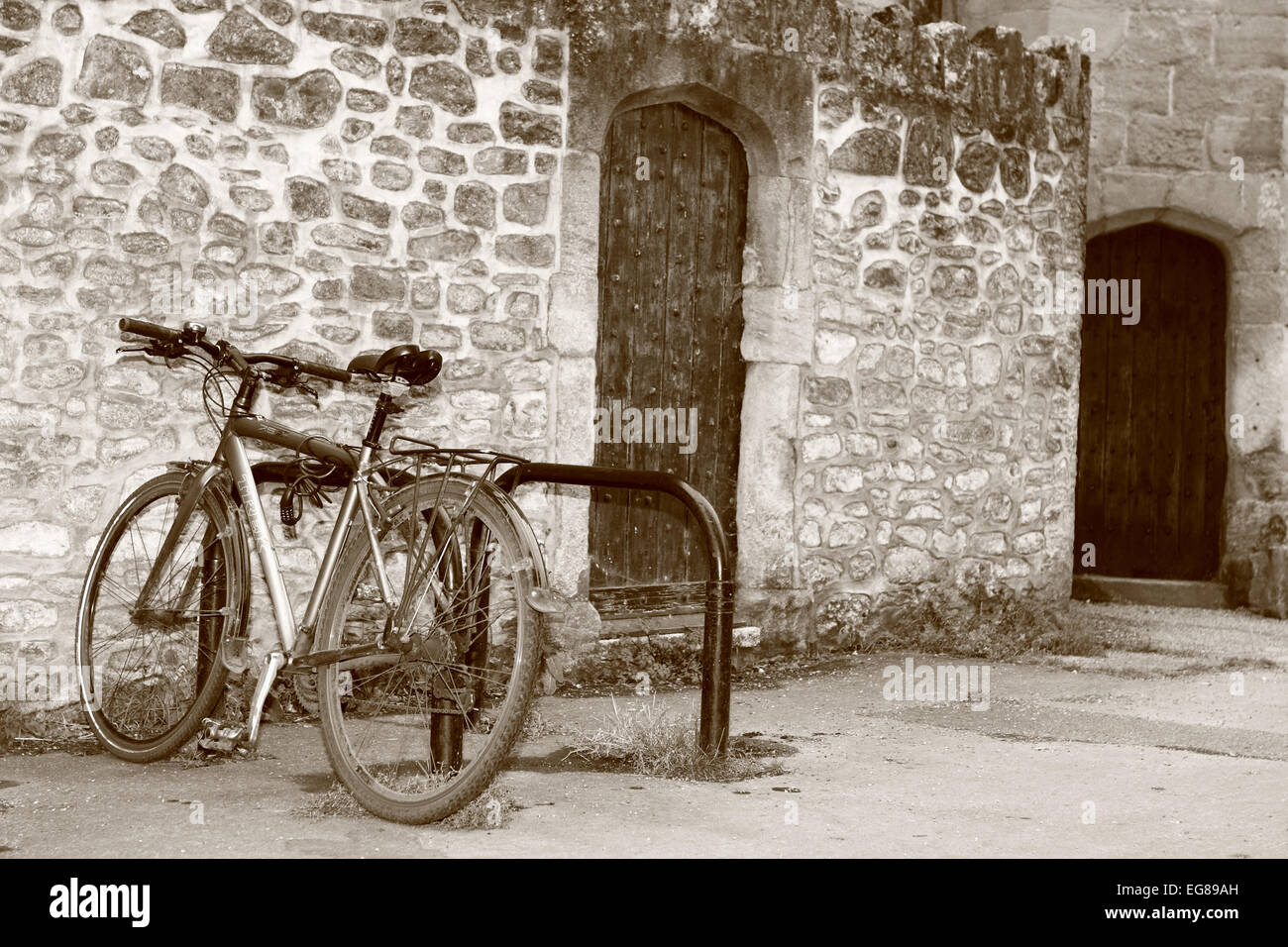 A bicycle locked to a cycle rack next to an old stone wall and wooden door in Wells, Somerset, England Stock Photo
