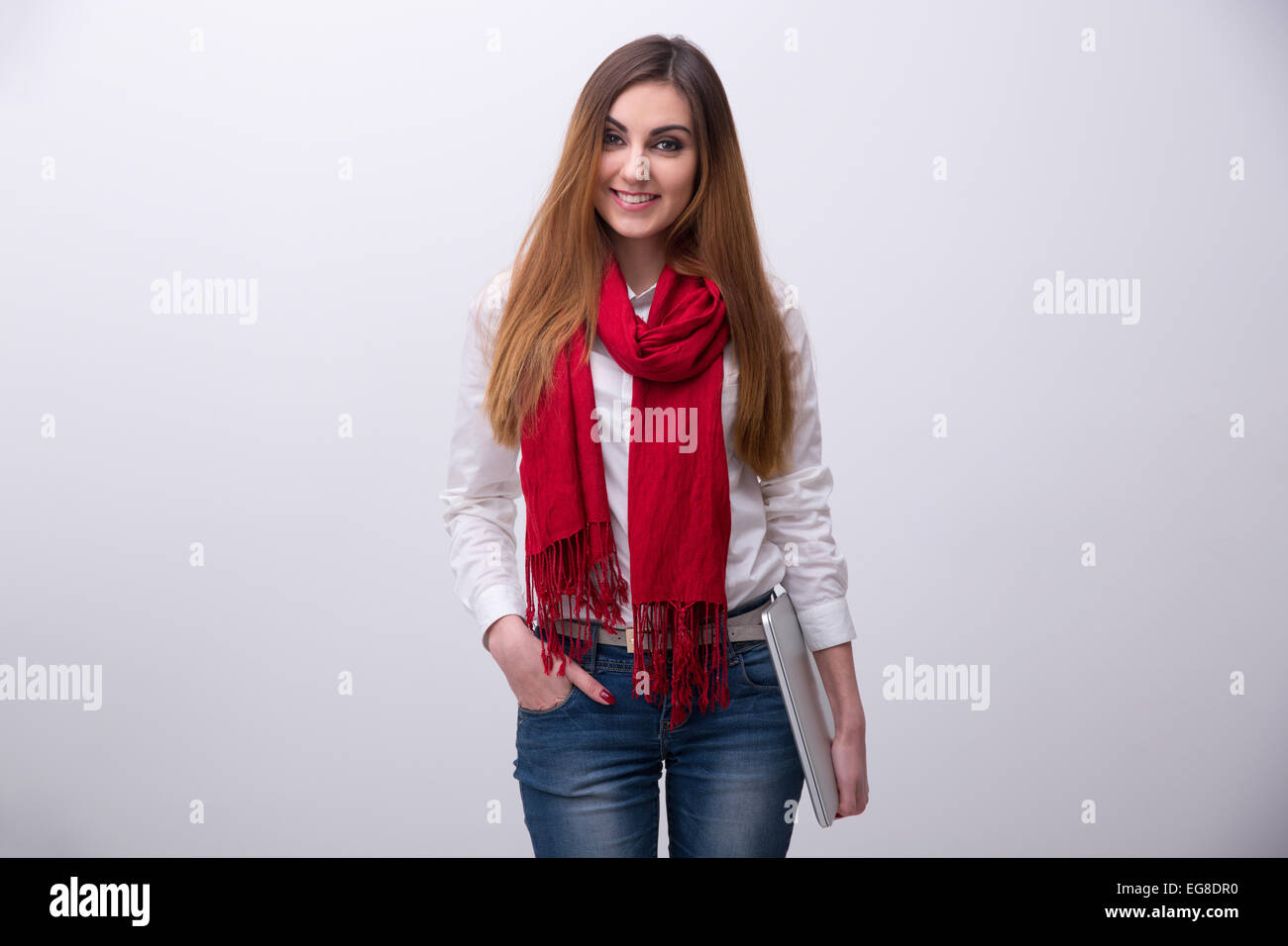 Portrait of a smiling young student standing with laptop over gray ...
