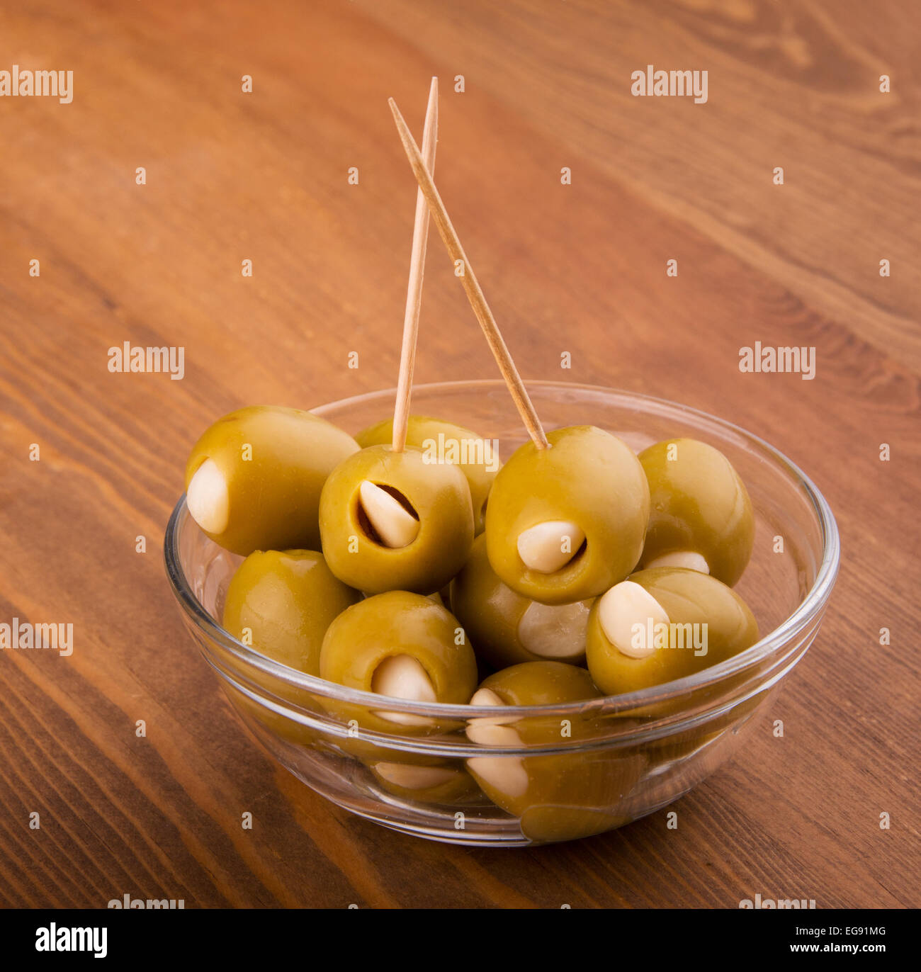 Green garlic stuffed olives in a glass bowl on dark wood table Stock