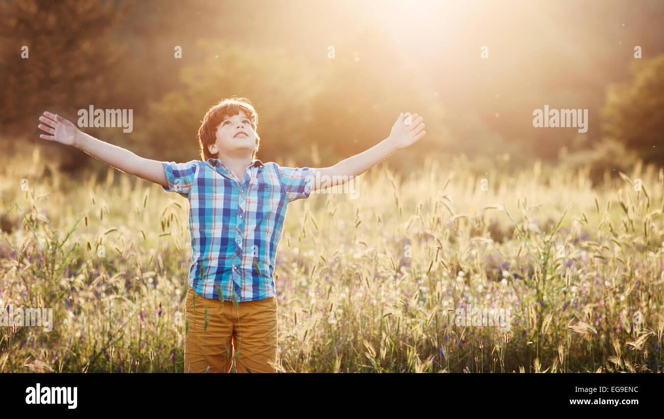 Boy (8-9) in meadow with arms outstretched looking up Stock Photo