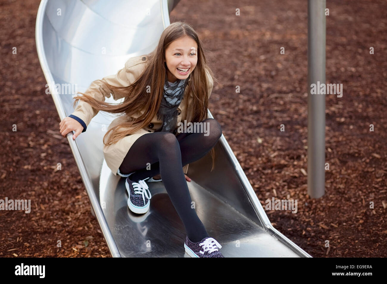 Happy teenage girl messing about on a slide in a playground Stock Photo