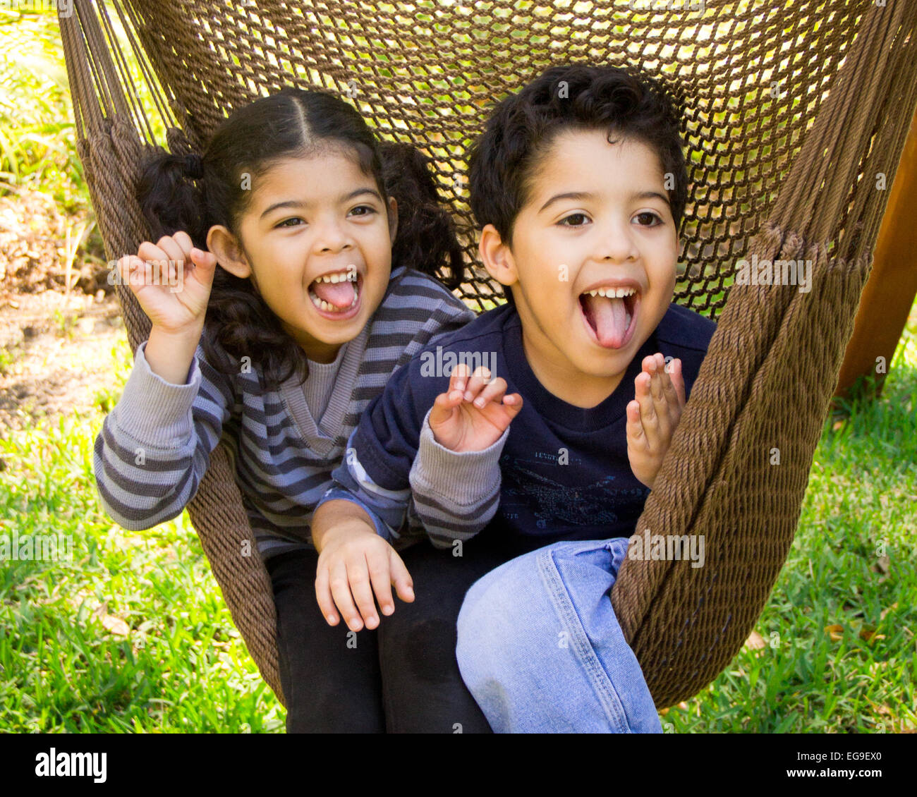 Twin brother and sister sitting in a hammock pulling funny faces Stock Photo