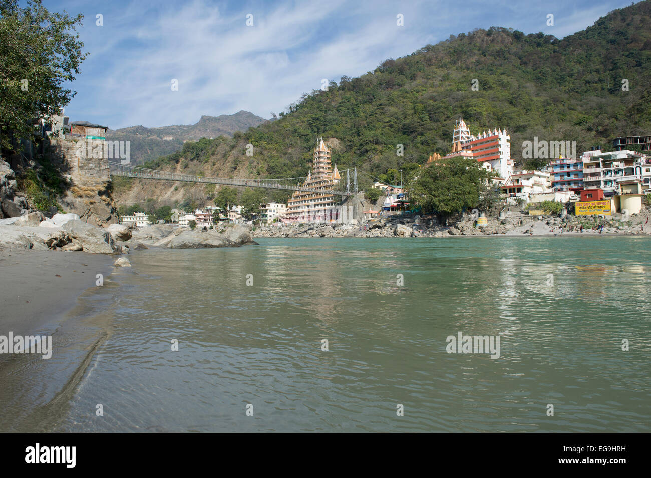 A view from the beach with the Temples and mountains of Rishikesh with Lakshman Jhula bridge crossing the Ganges or Ganga river. Stock Photo