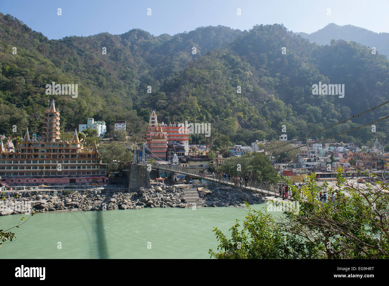 The Temples and mountains of Rishikesh with Lakshman Jhula bridge in the foreground which crosses the Ganges or Ganga river. Stock Photo