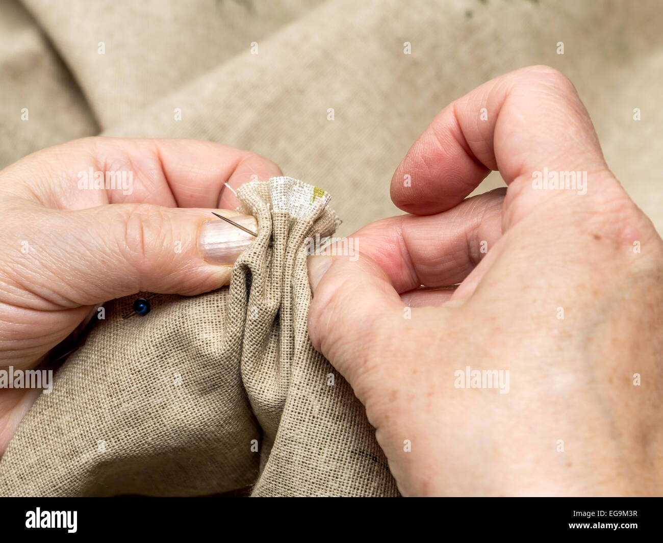 Closeup of senior woman's hands basting linen border with needle and thread Stock Photo