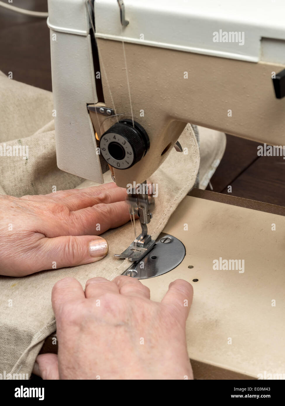 Closeup of senior woman's hands sawing linen border with sewing machine Stock Photo